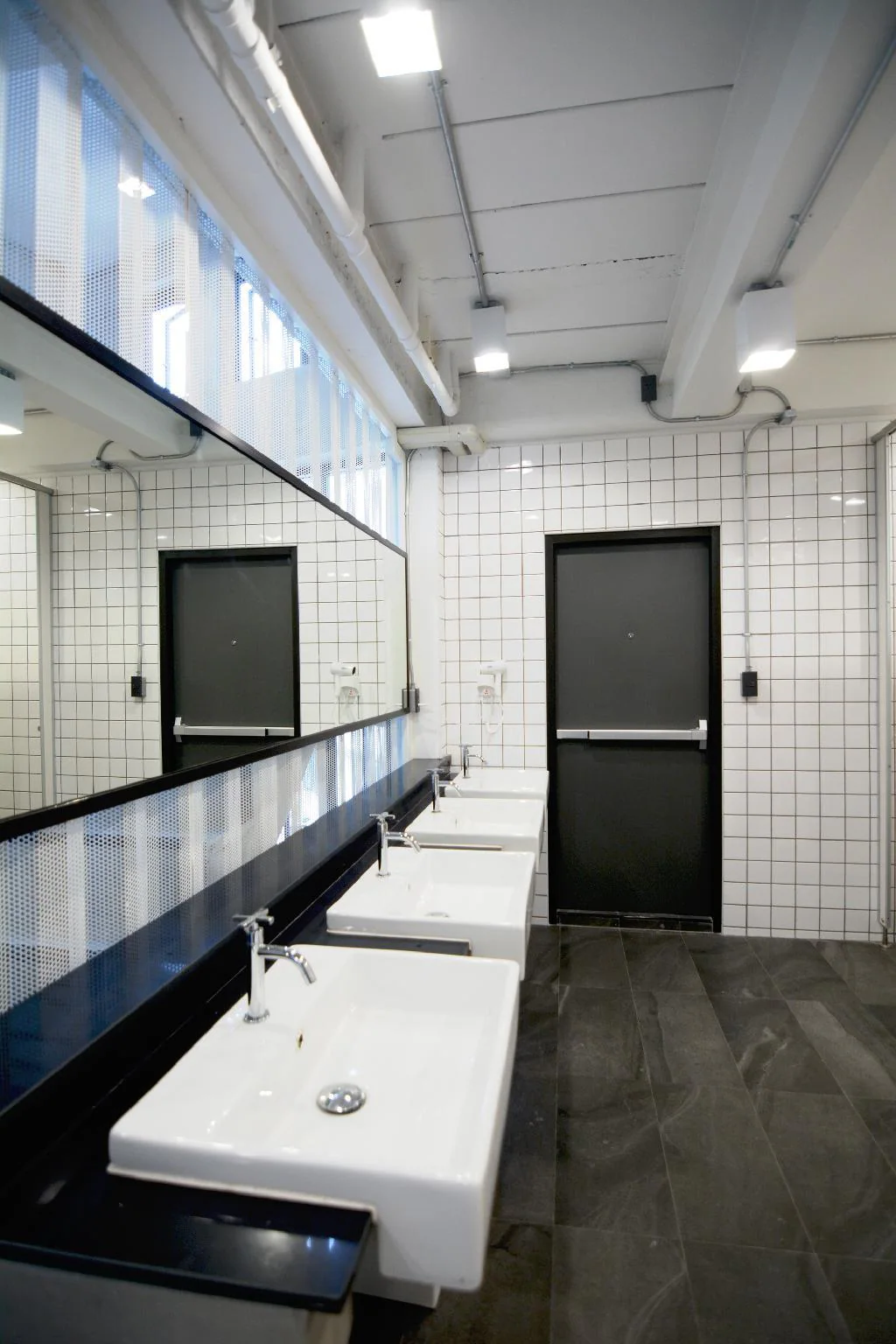Shared bathroom with white tiles, black doors and a row of sinks