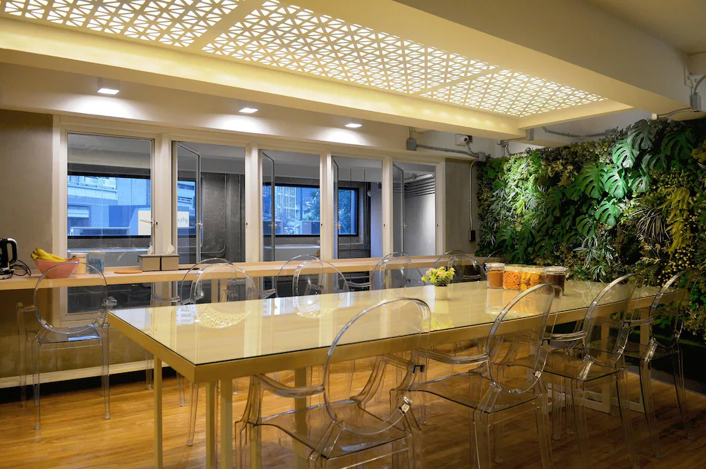 Common dining room with a long glass table and a living green wall