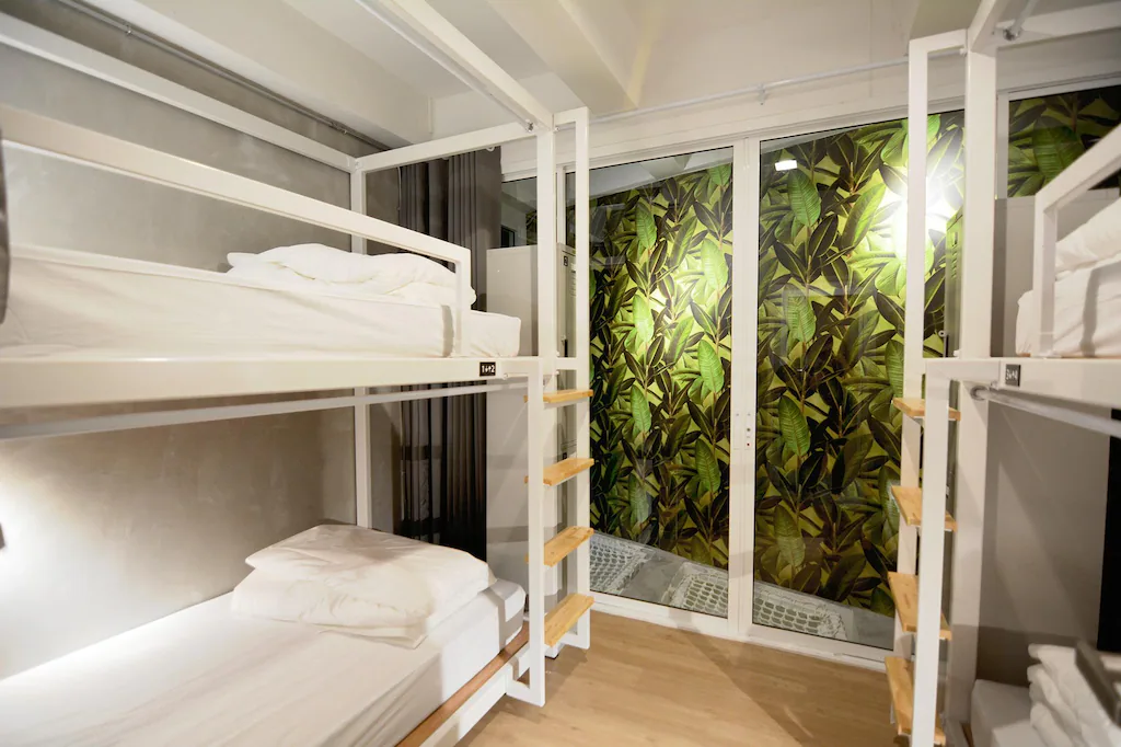 Mixed dorm with white bunk capsules, wooden ladders and a leaf-print wall