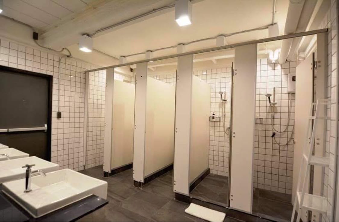 Clean shared shower stalls with white tiles and private dividers